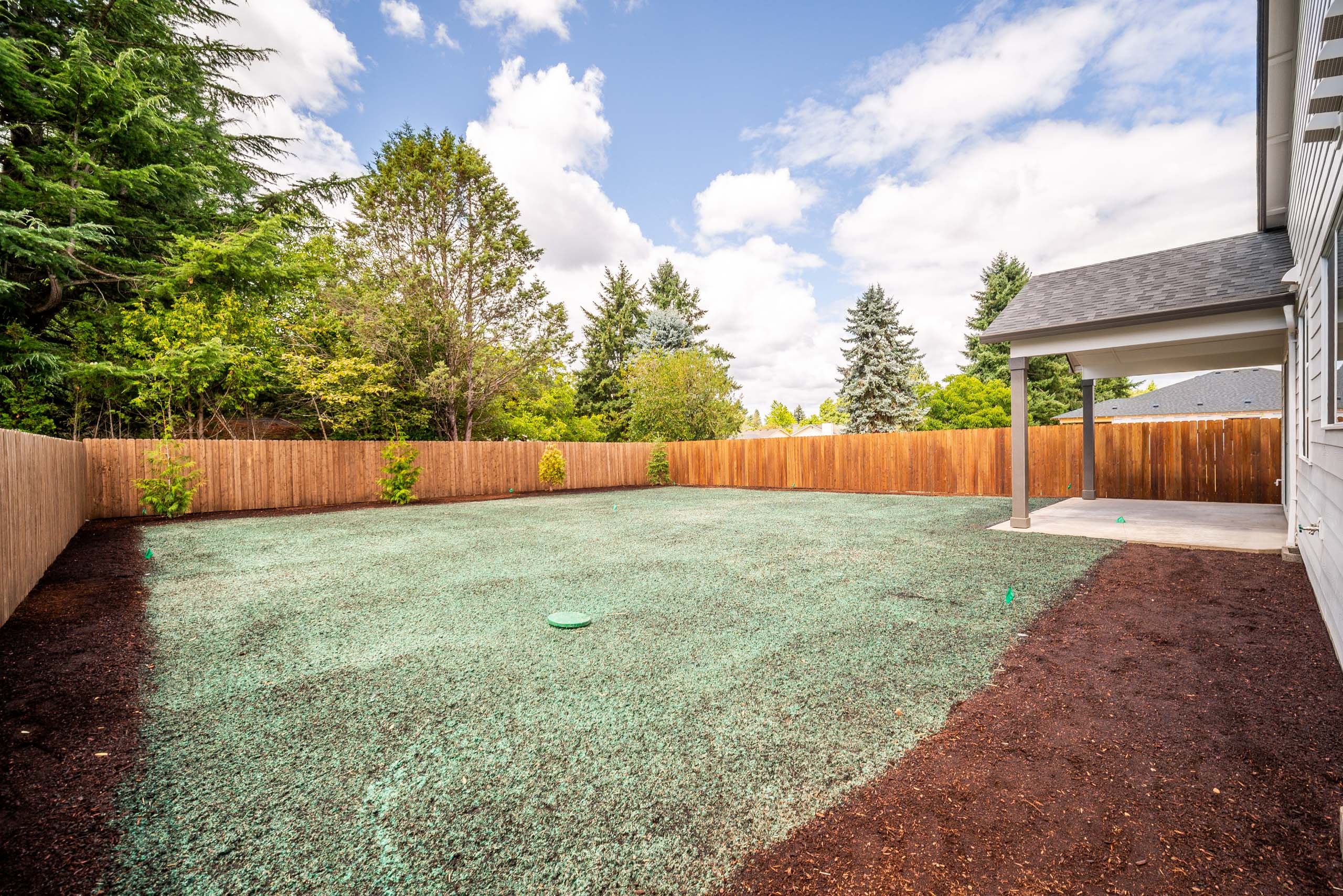 A backyard with a gravel area and a wooden pergola under a blue sky.