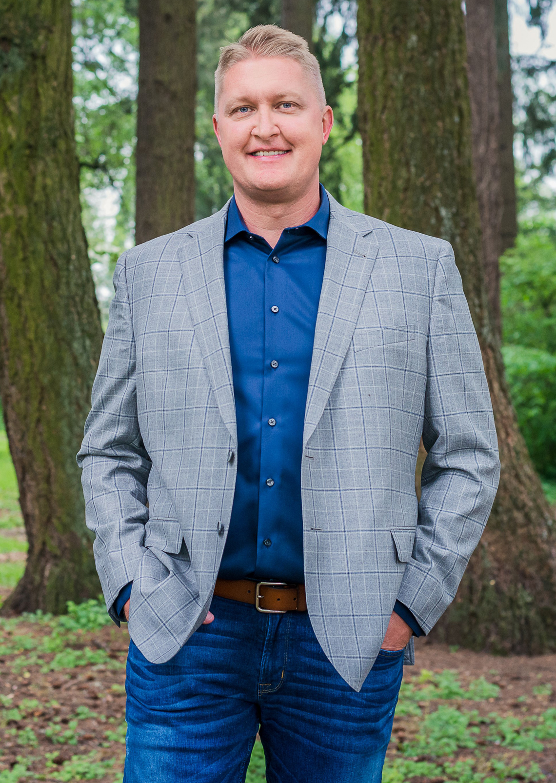 Smiling man in a gray blazer and blue shirt outdoors.