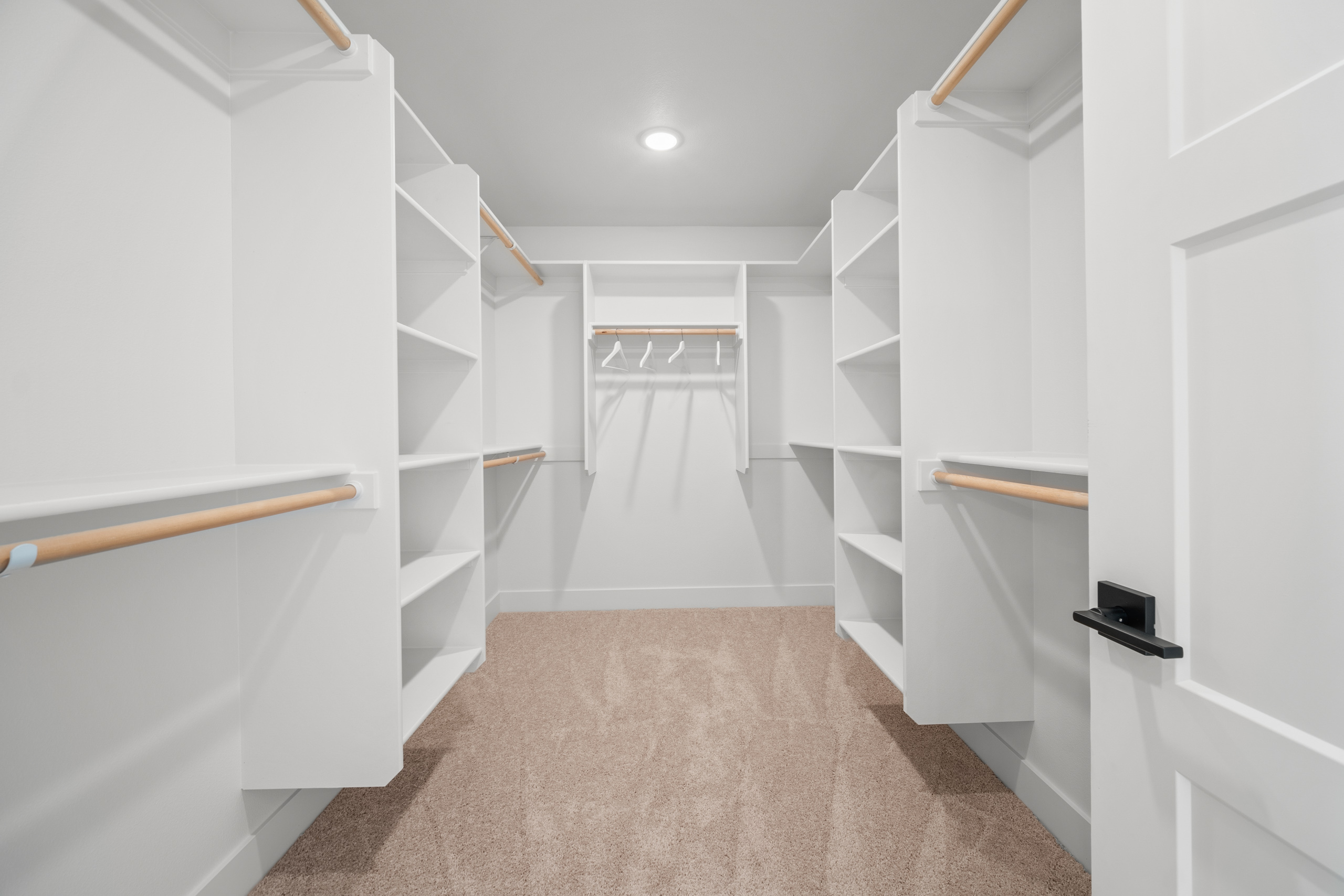 Spacious walk-in closet with white shelving and wooden floor.
