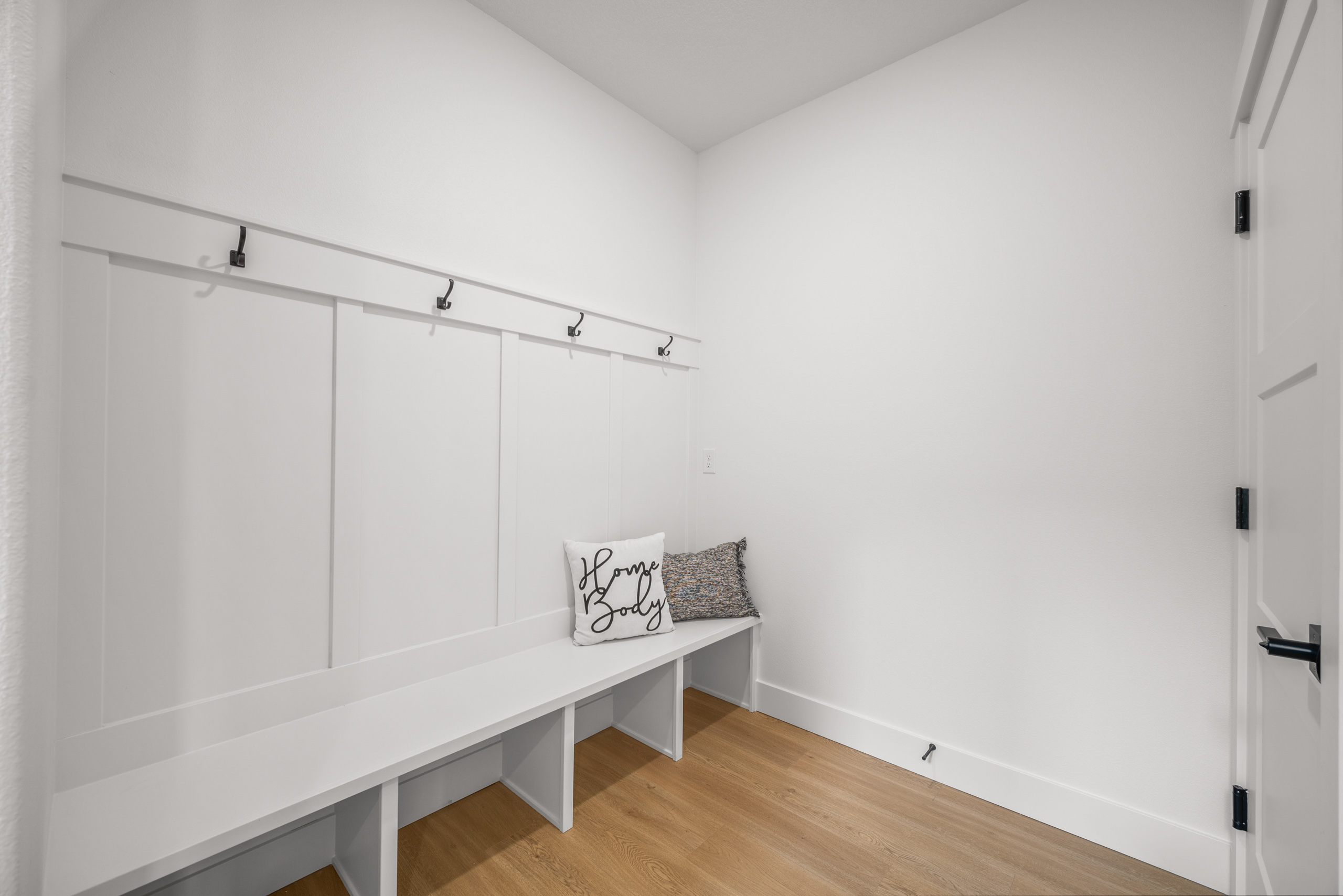 Minimalist white mudroom with bench, hooks, and storage cubbies.