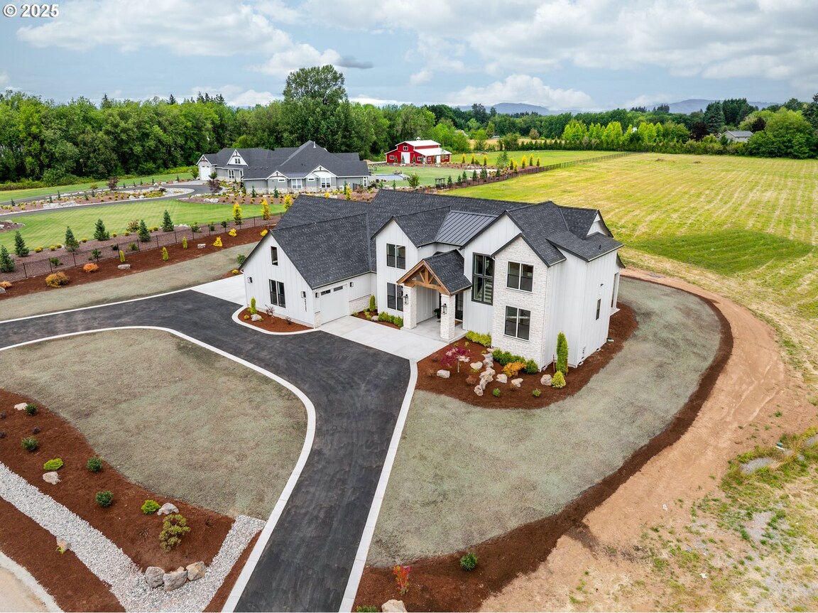 A large, modern farmhouse with a spacious driveway and green lawn.