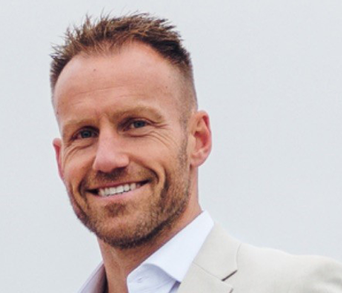 Man in a light beige suit smiling warmly.